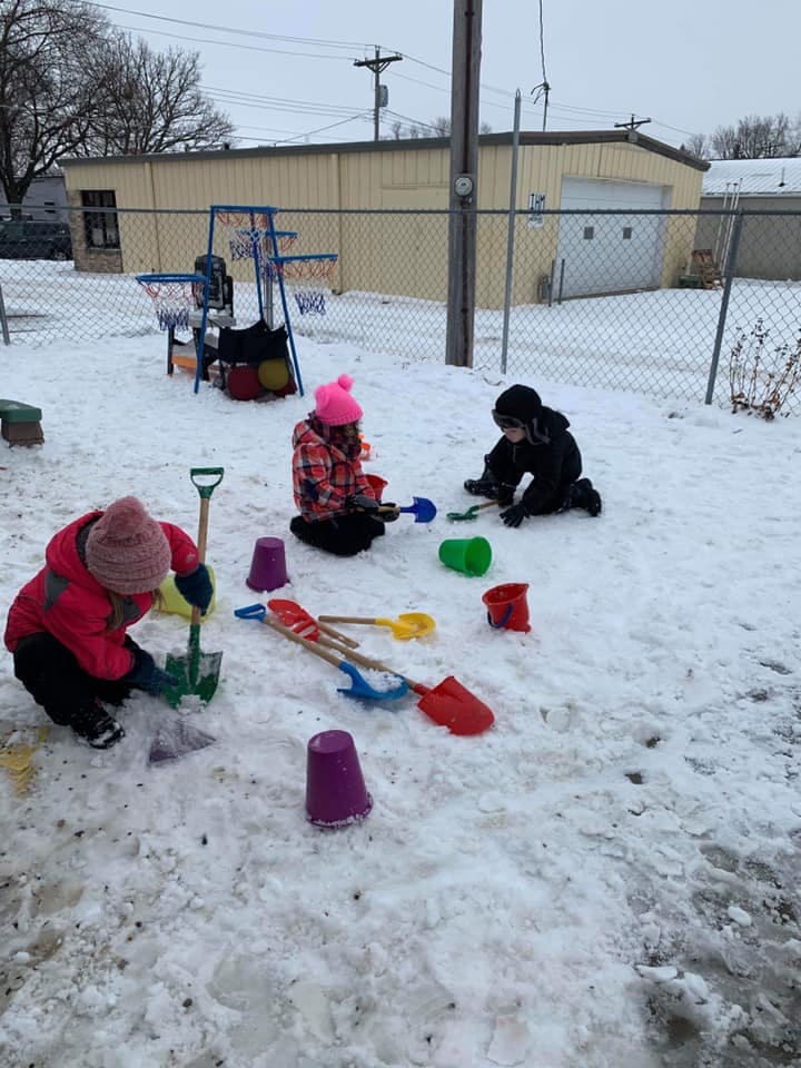 Three children playing in snow with shovels and buckets