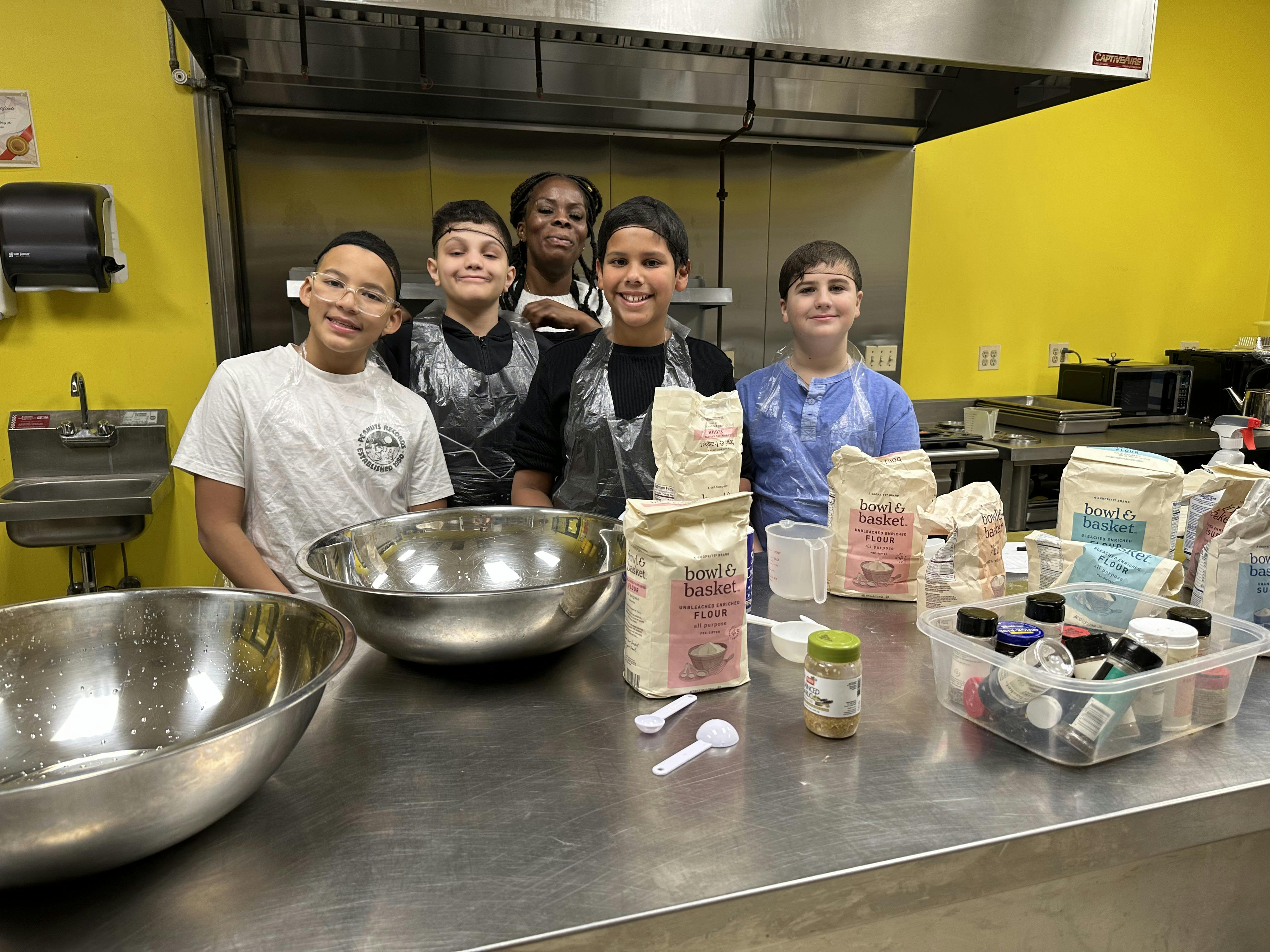 Four children and an adult standing in a kitchen with flour and bowls