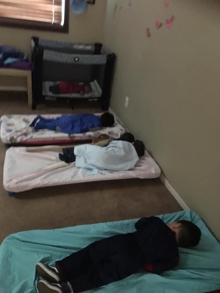 Multiple children sleeping on mats and in a playpen