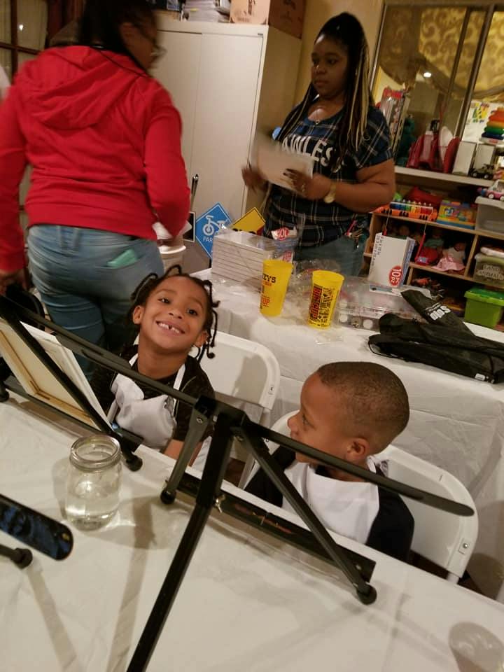 Two children seated at a table with two adults standing behind them