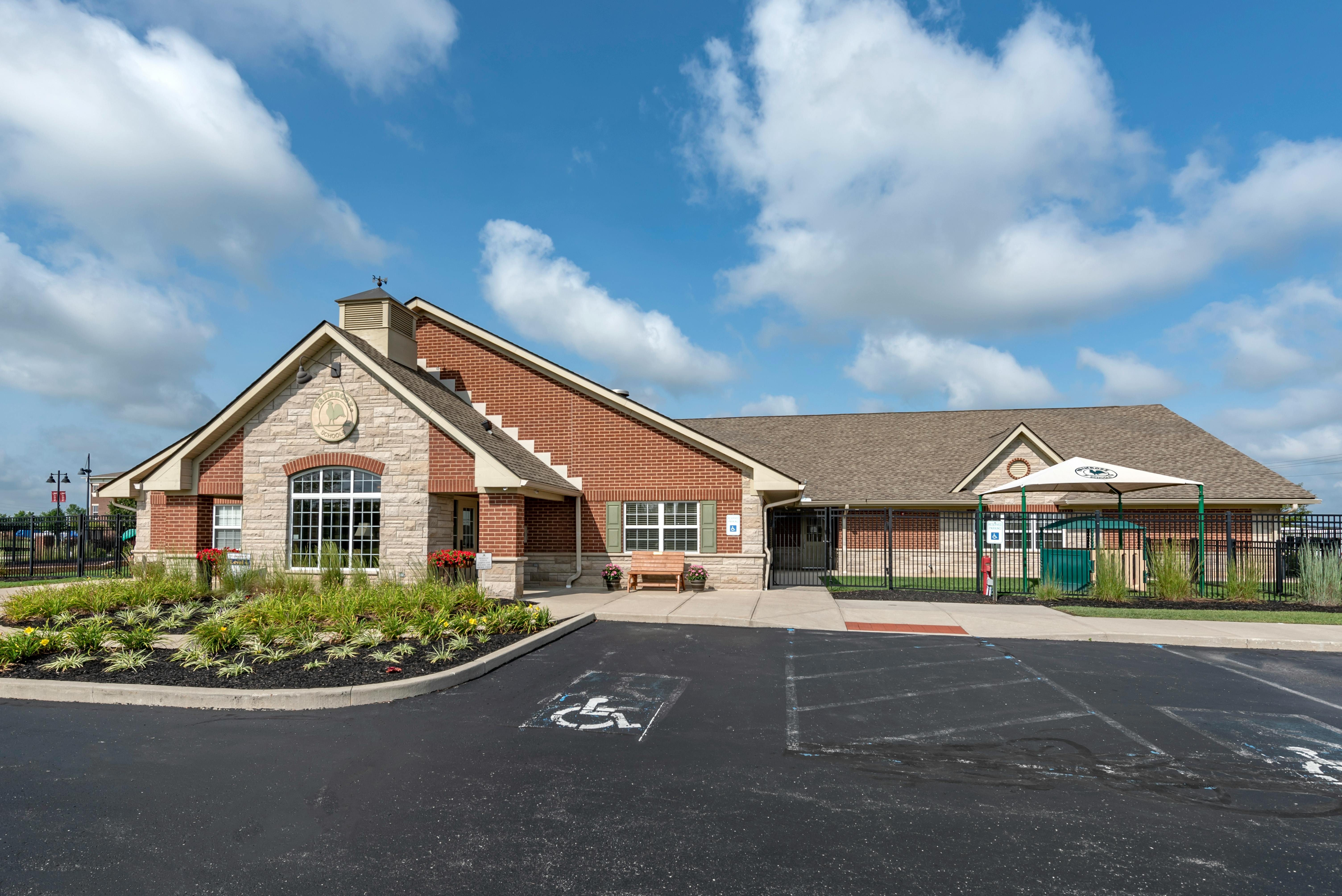 A low brick and stone school building with a small parking lot and landscaping