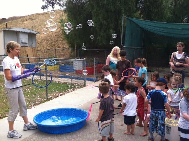 Person making bubbles with a large wand for a group of children