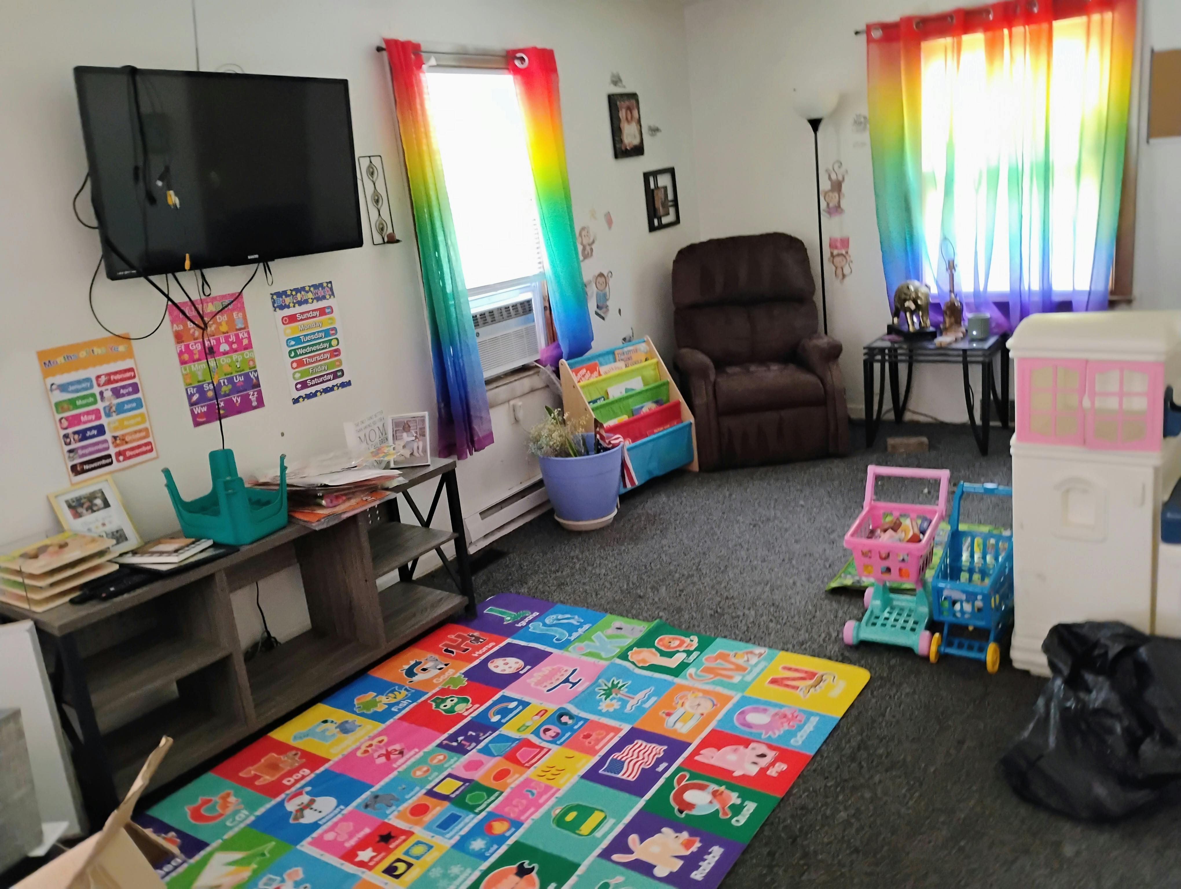 A playroom with a television, colorful rug, shelves of toys, and rainbow curtains