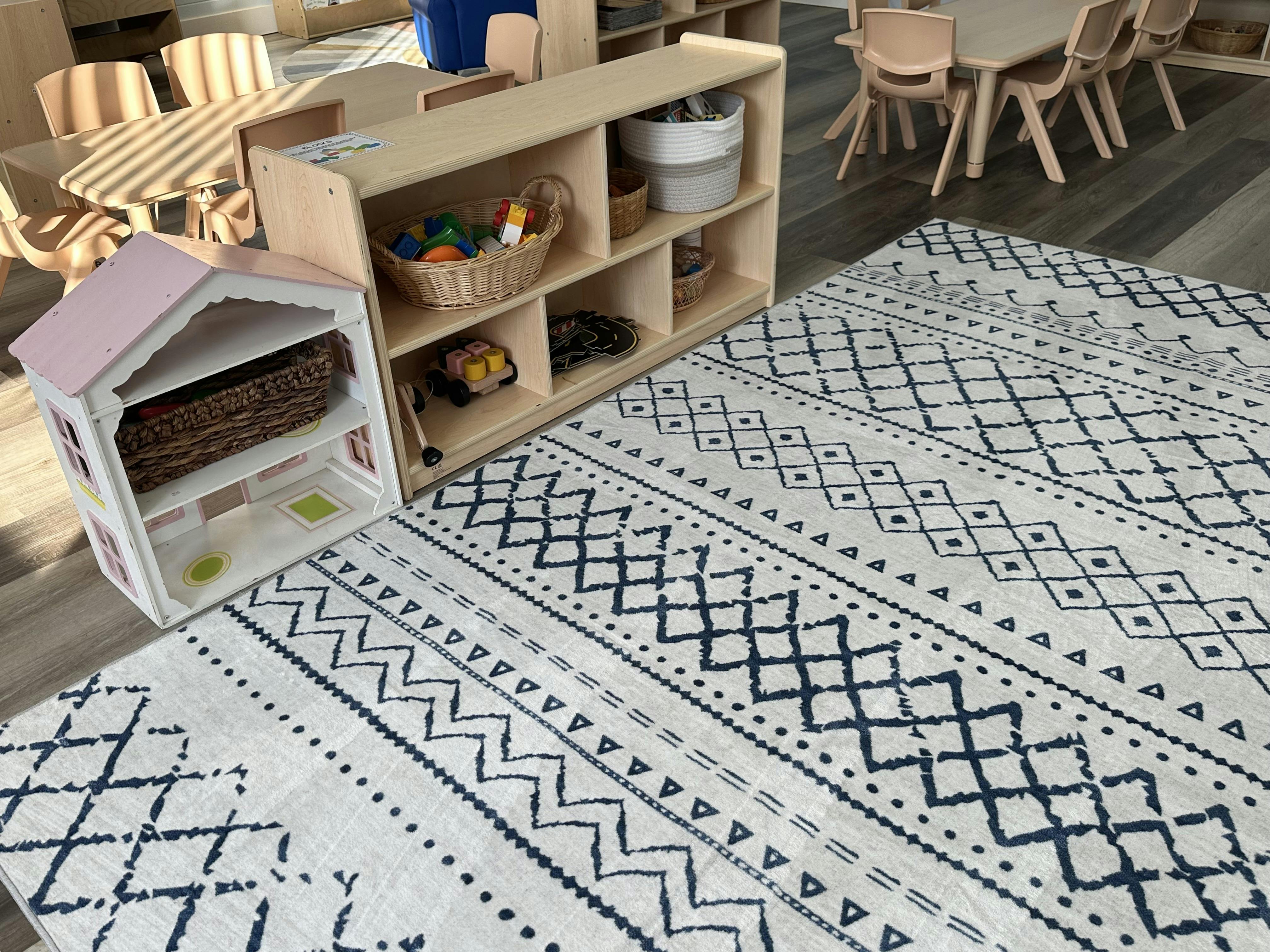 Playroom with a patterned rug, wooden shelves, and a dollhouse