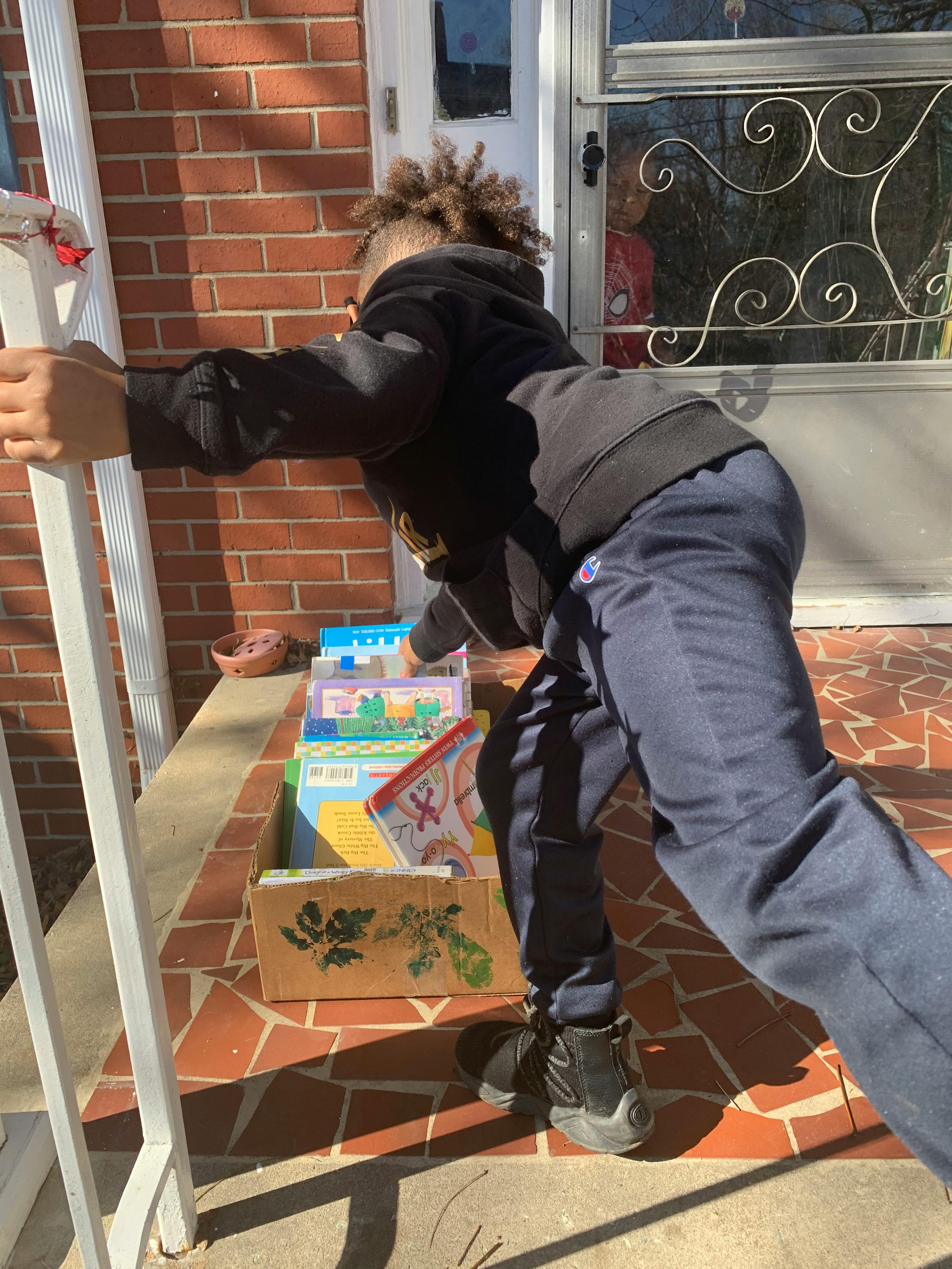 Child reaching into a box of books on a porch