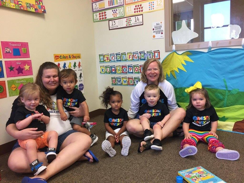 Two adults and five children sitting on the floor in a classroom