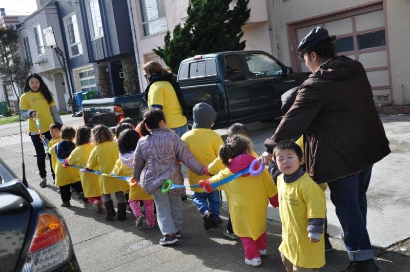 Adults walking with a line of children holding onto a rope