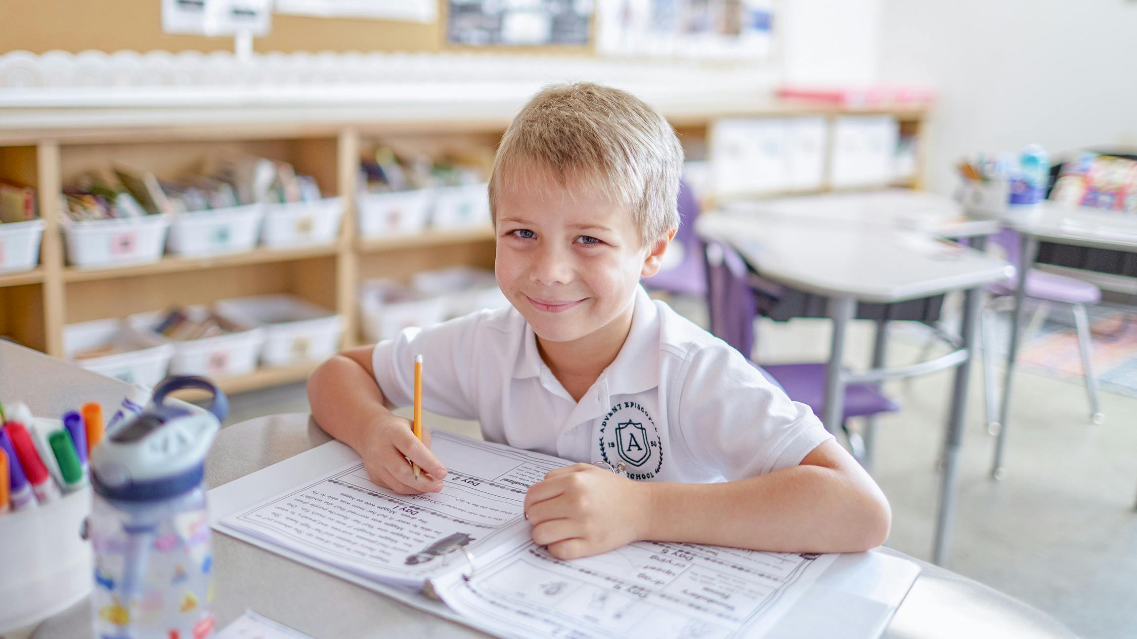 Child writing in a notebook at a desk in a classroom