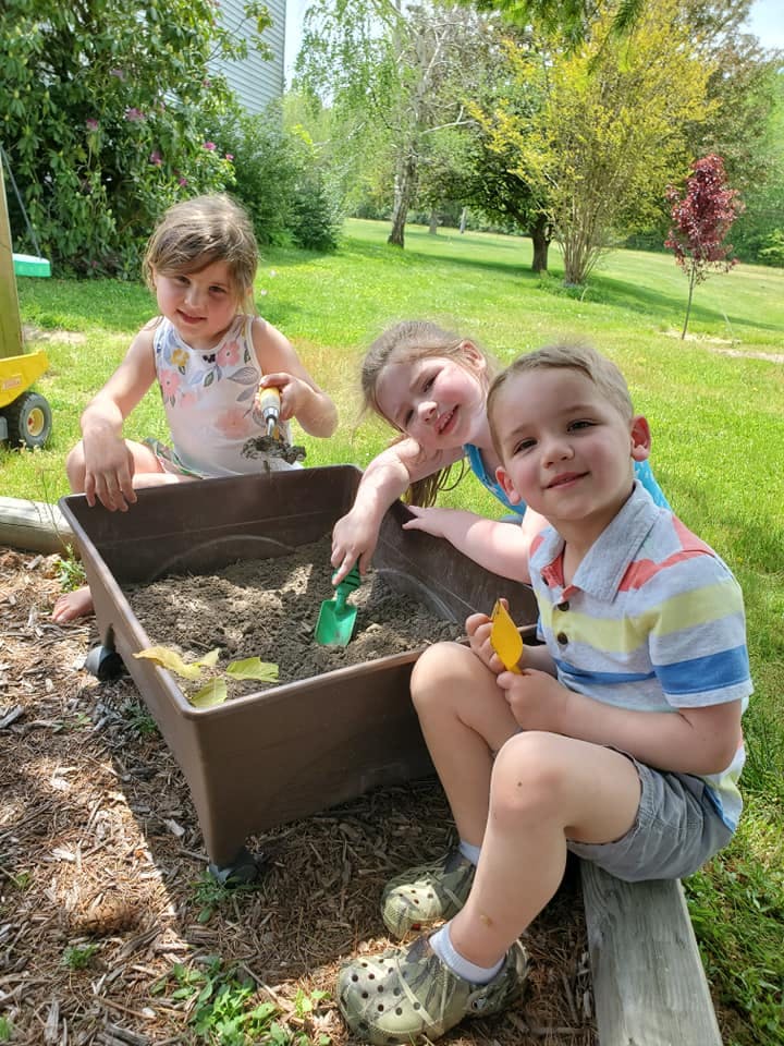 Three children playing in a sandbox with shovels