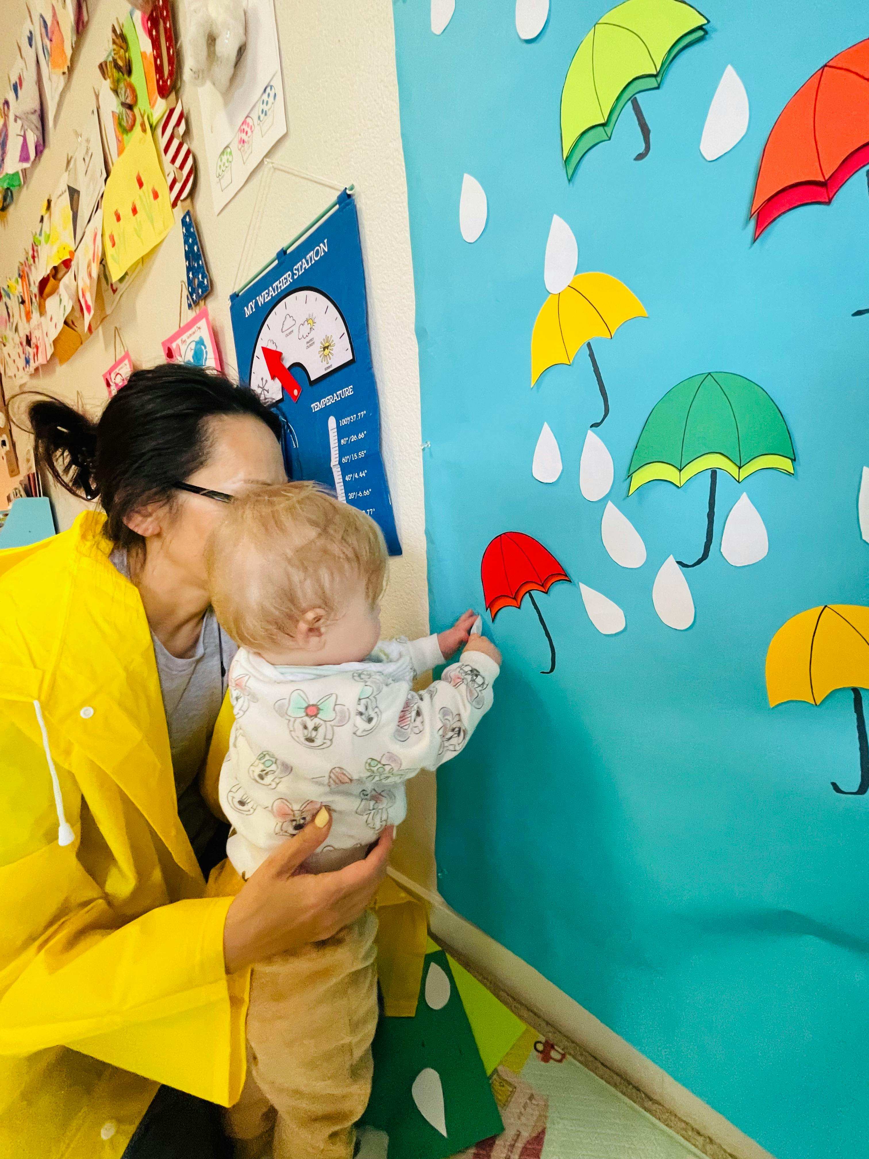 Person holding a child who is touching a paper umbrella on a blue wall