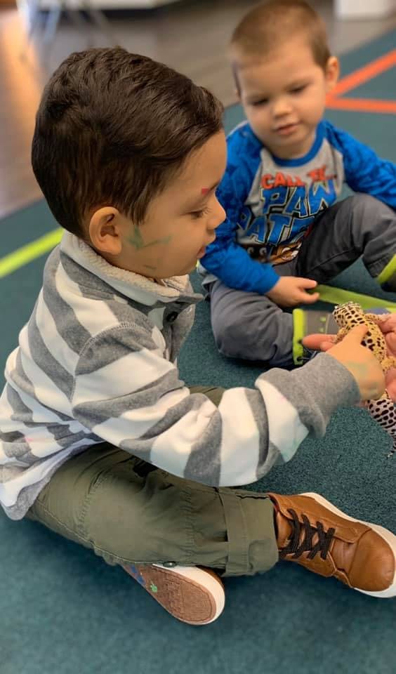 Child holding a gecko while another child watches