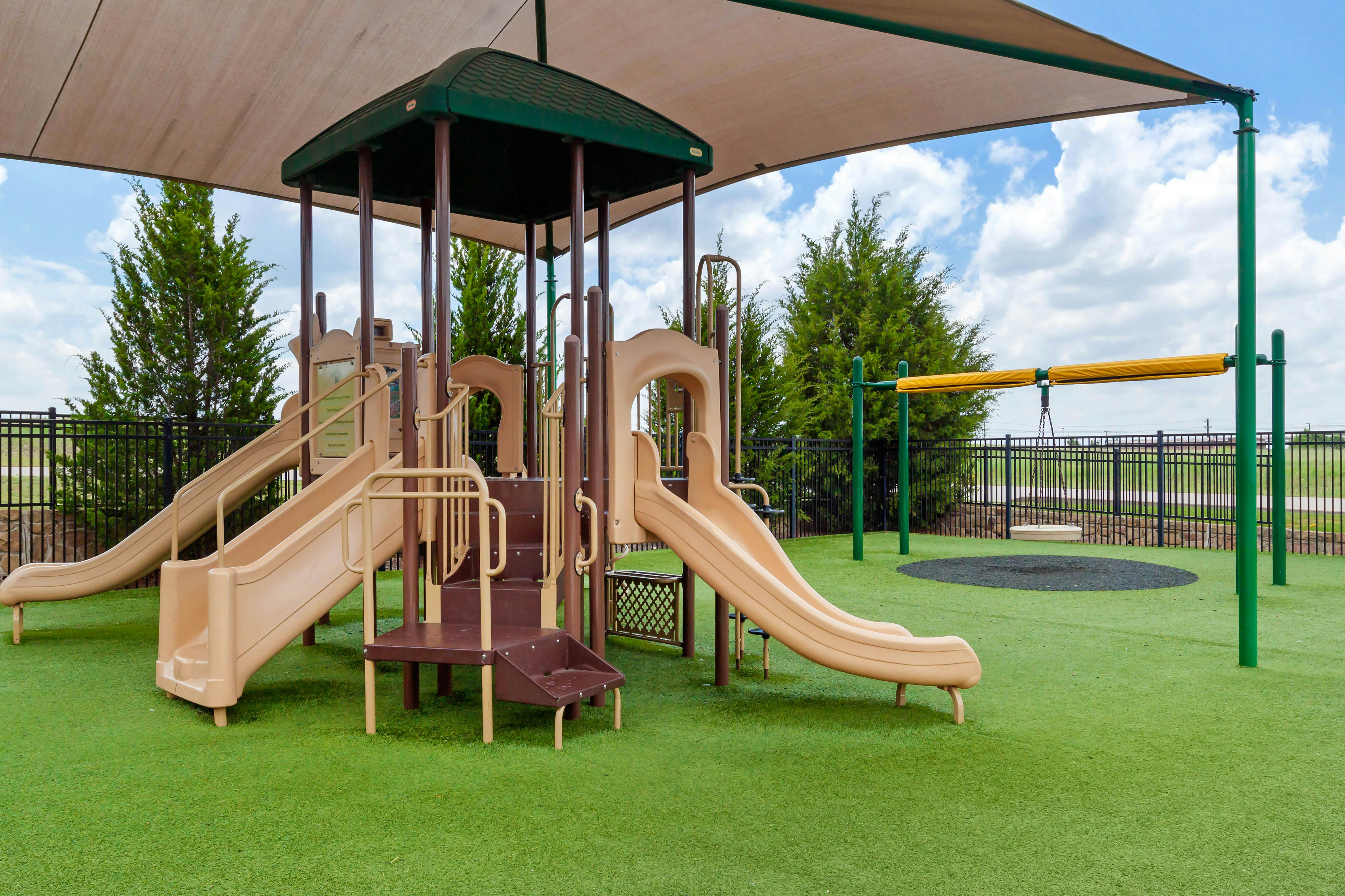 Empty playground with tan and brown playset, slides, and swing on green turf