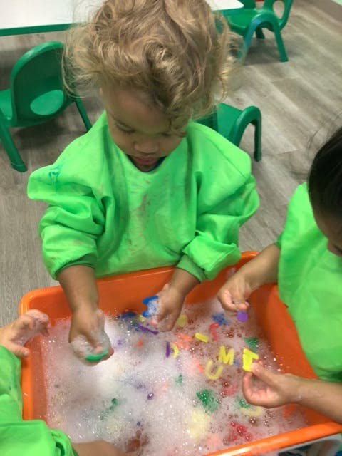 Child playing with letters in a tub of soapy water