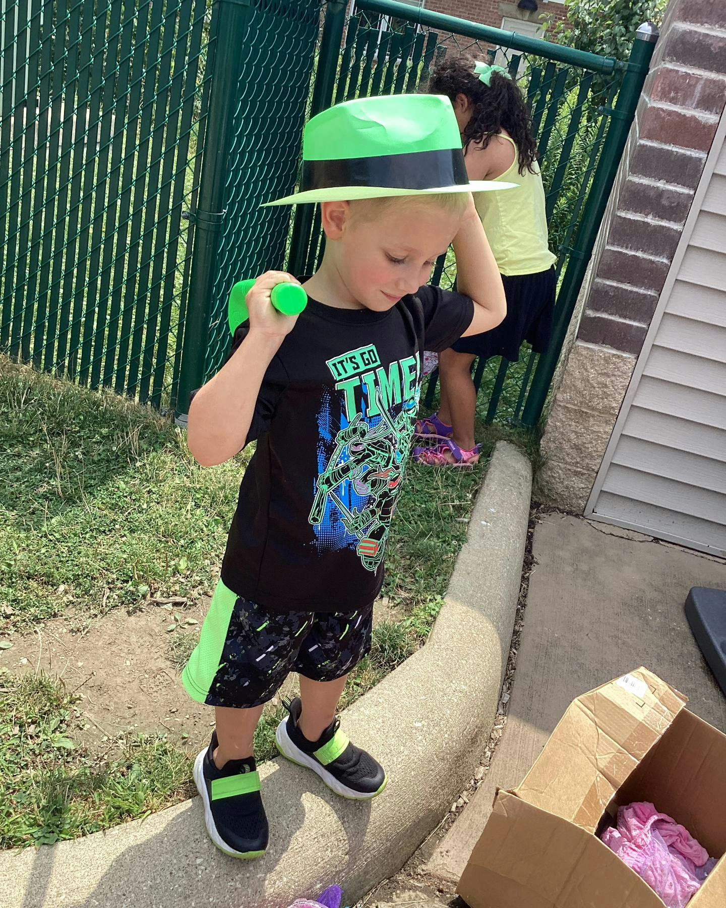 Child in a green hat and black shirt holding a green object