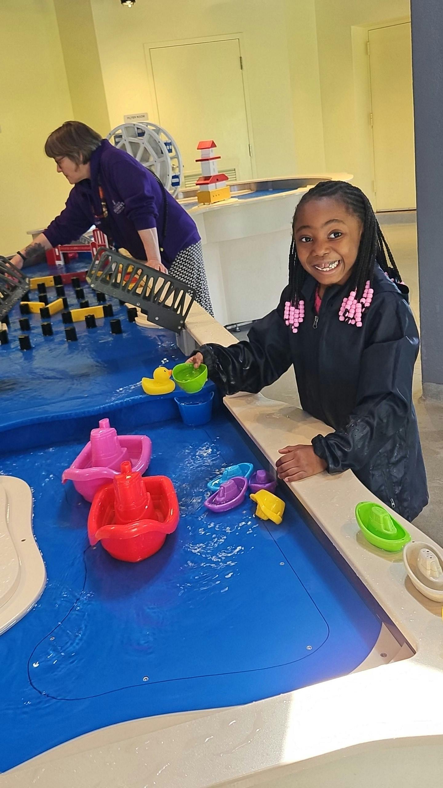 Child in rain jacket smiling while playing at a water table with small boats
