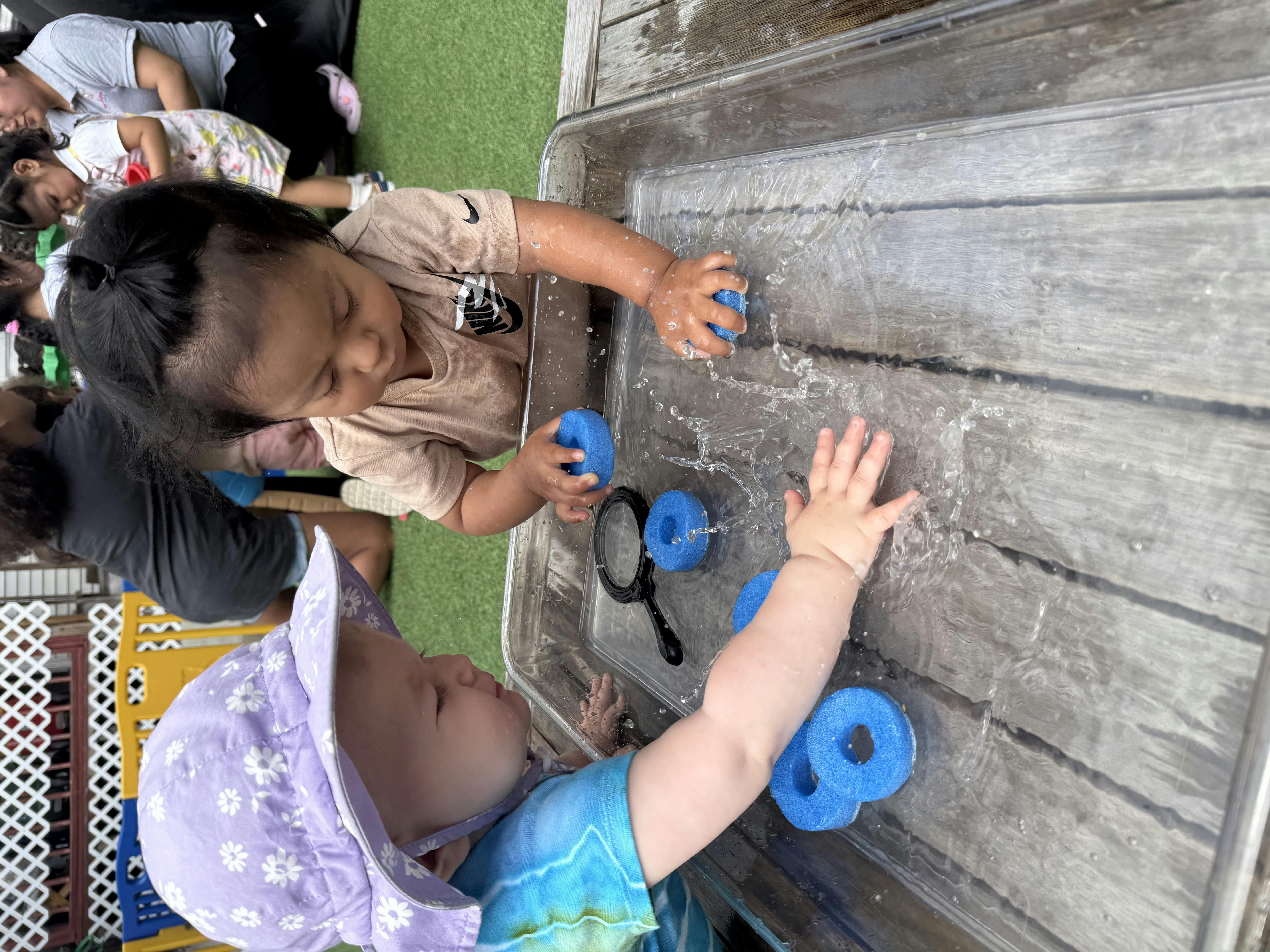 Two children playing with water and blue toys on a wooden surface
