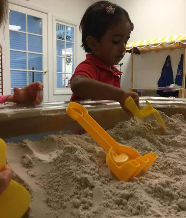 Child playing in sand with yellow sand toys