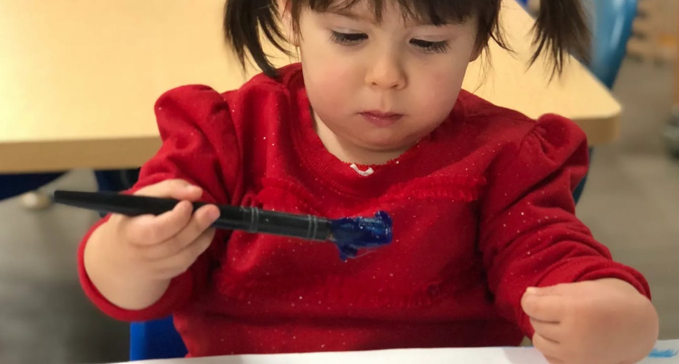 Child holding a paintbrush with blue paint