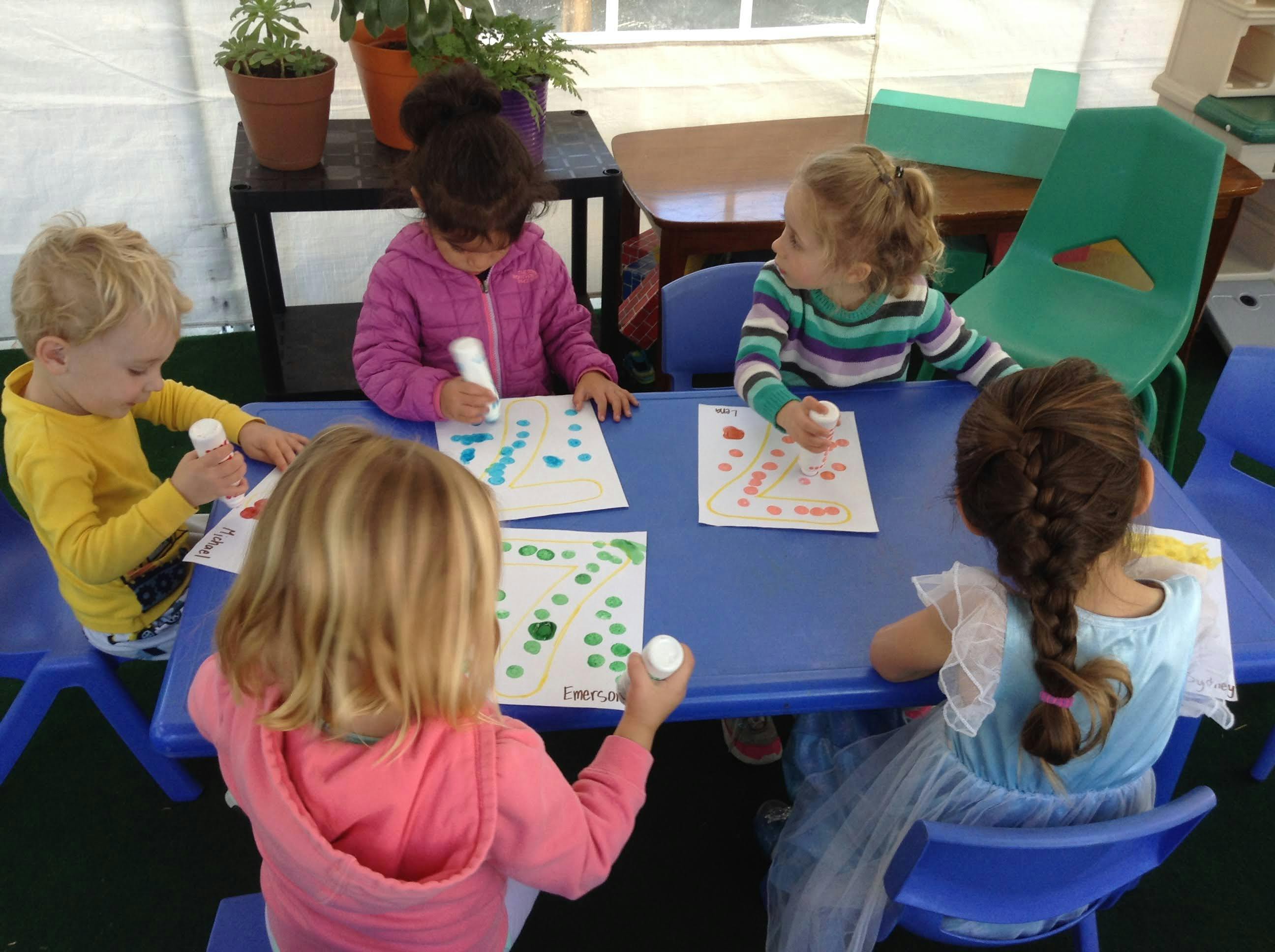 Four children sitting at a table doing crafts with dot markers on paper