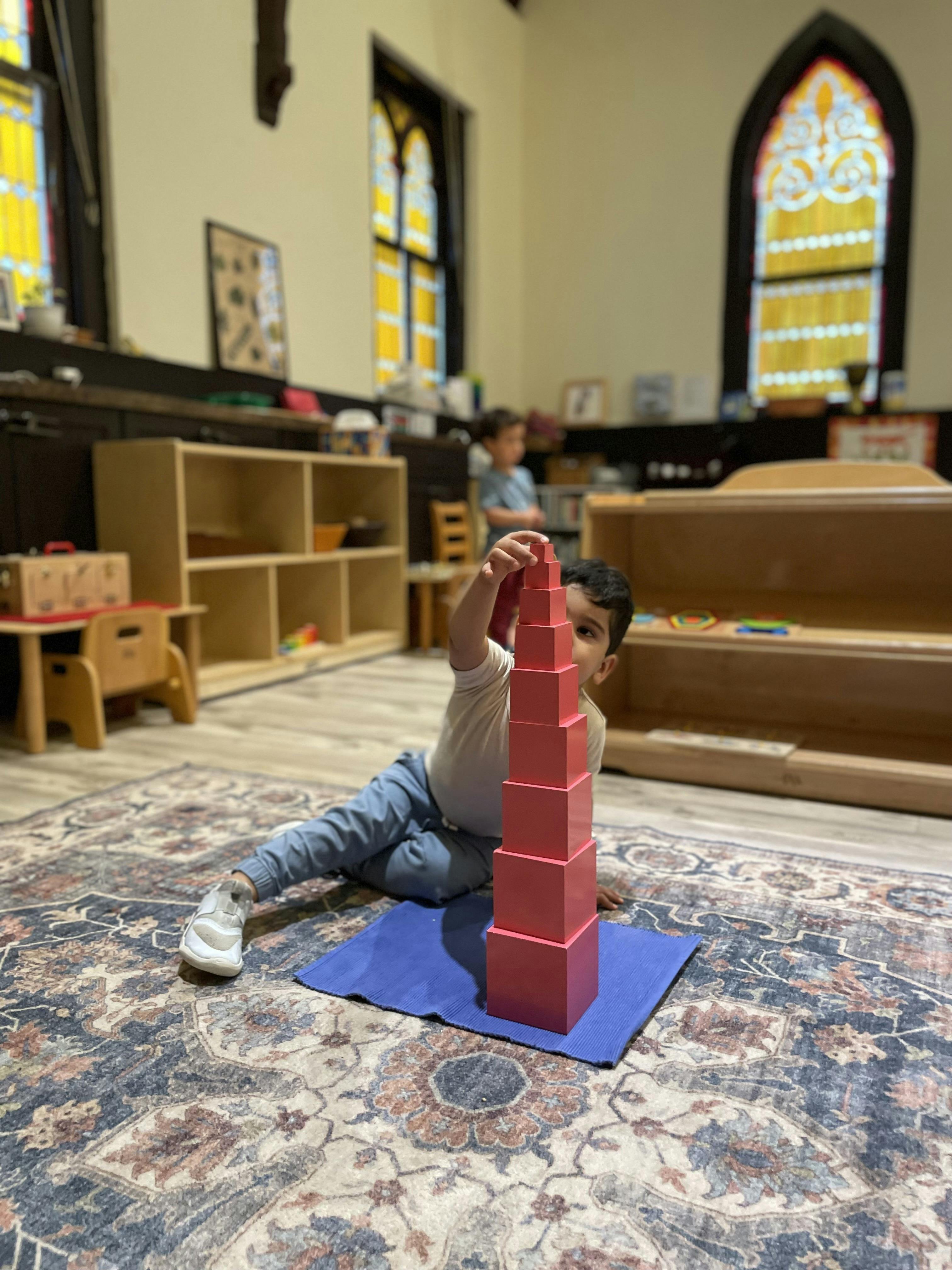 Child sitting on floor, stacking blocks in a classroom