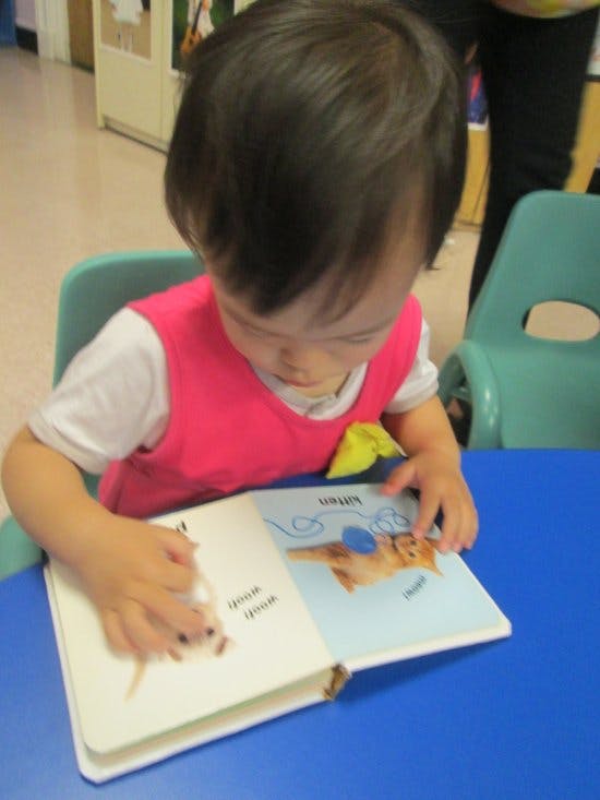 Child in a pink vest reading a book at a blue table
