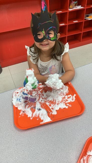 Child in a mask playing with shaving cream on a tray