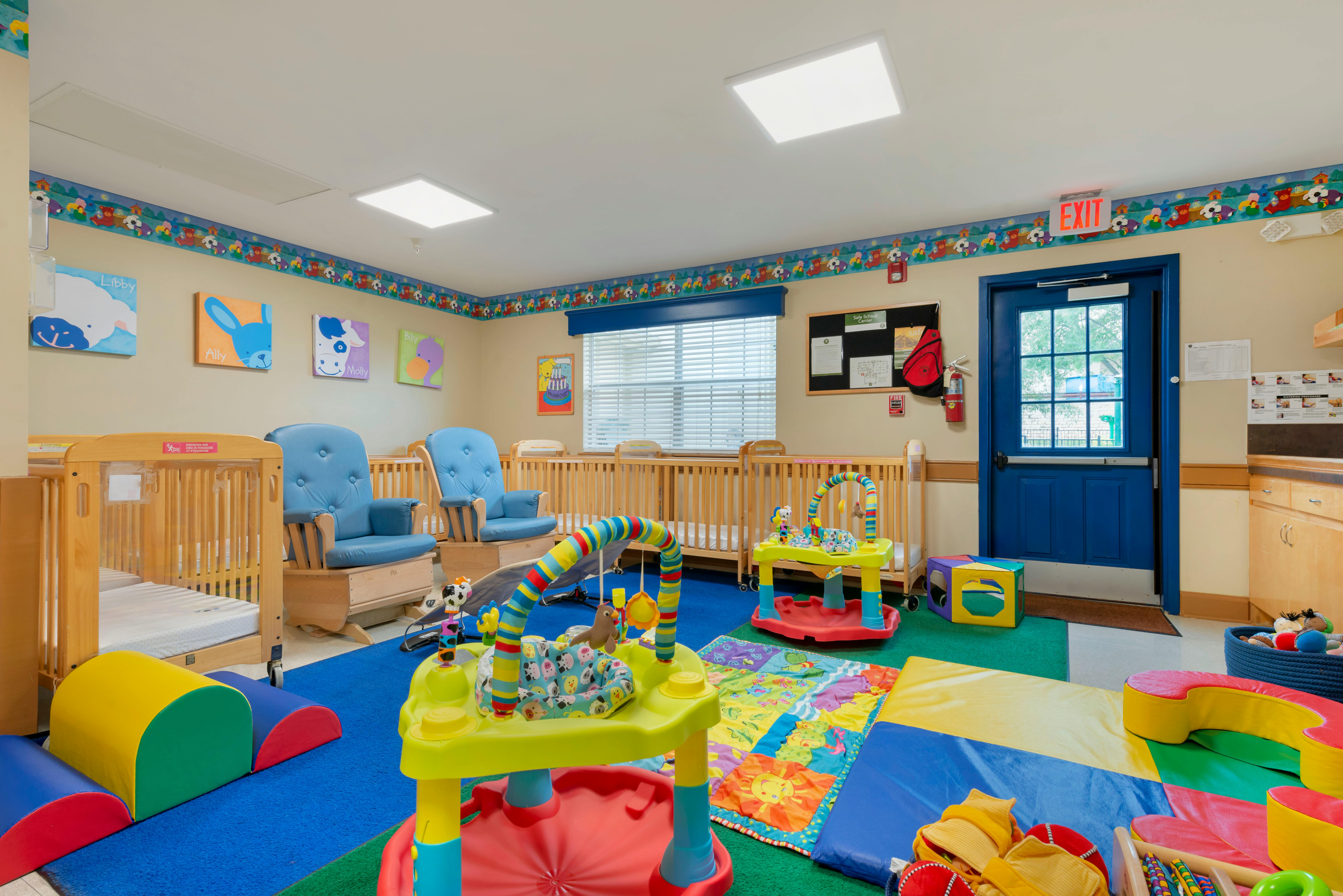 Baby room with multiple cribs, two blue rocking chairs, and colorful play mats and toys