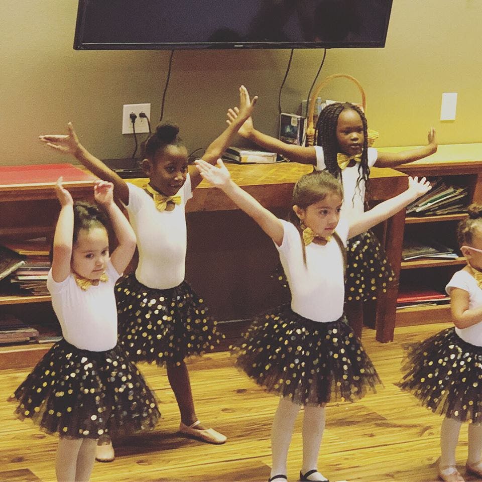 Children in tutus and leotards with arms raised