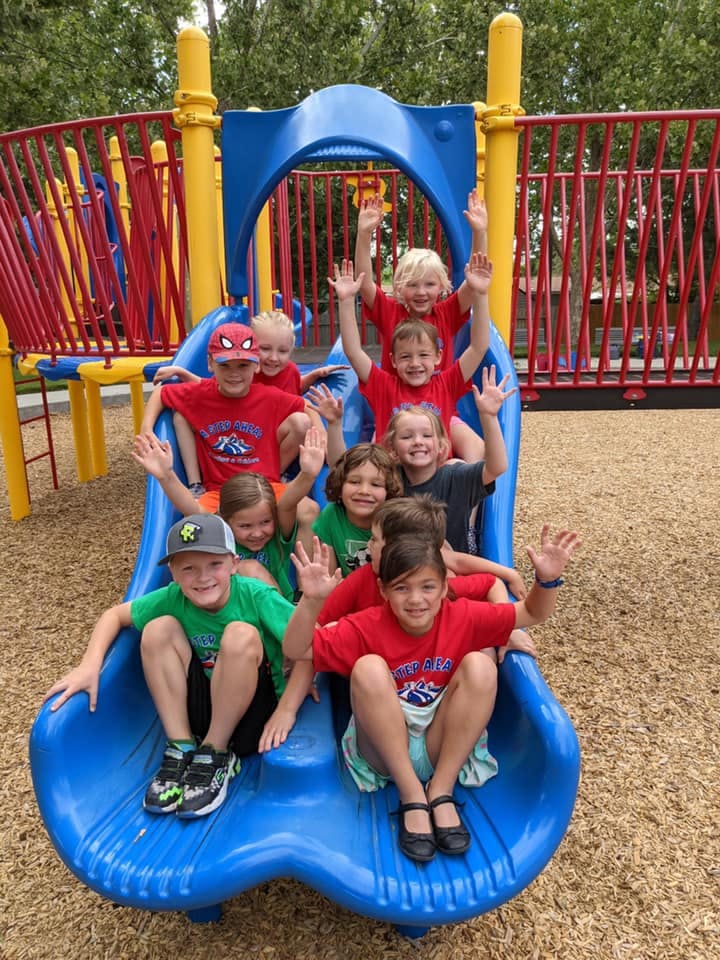 Group of children on a blue playground slide with hands raised