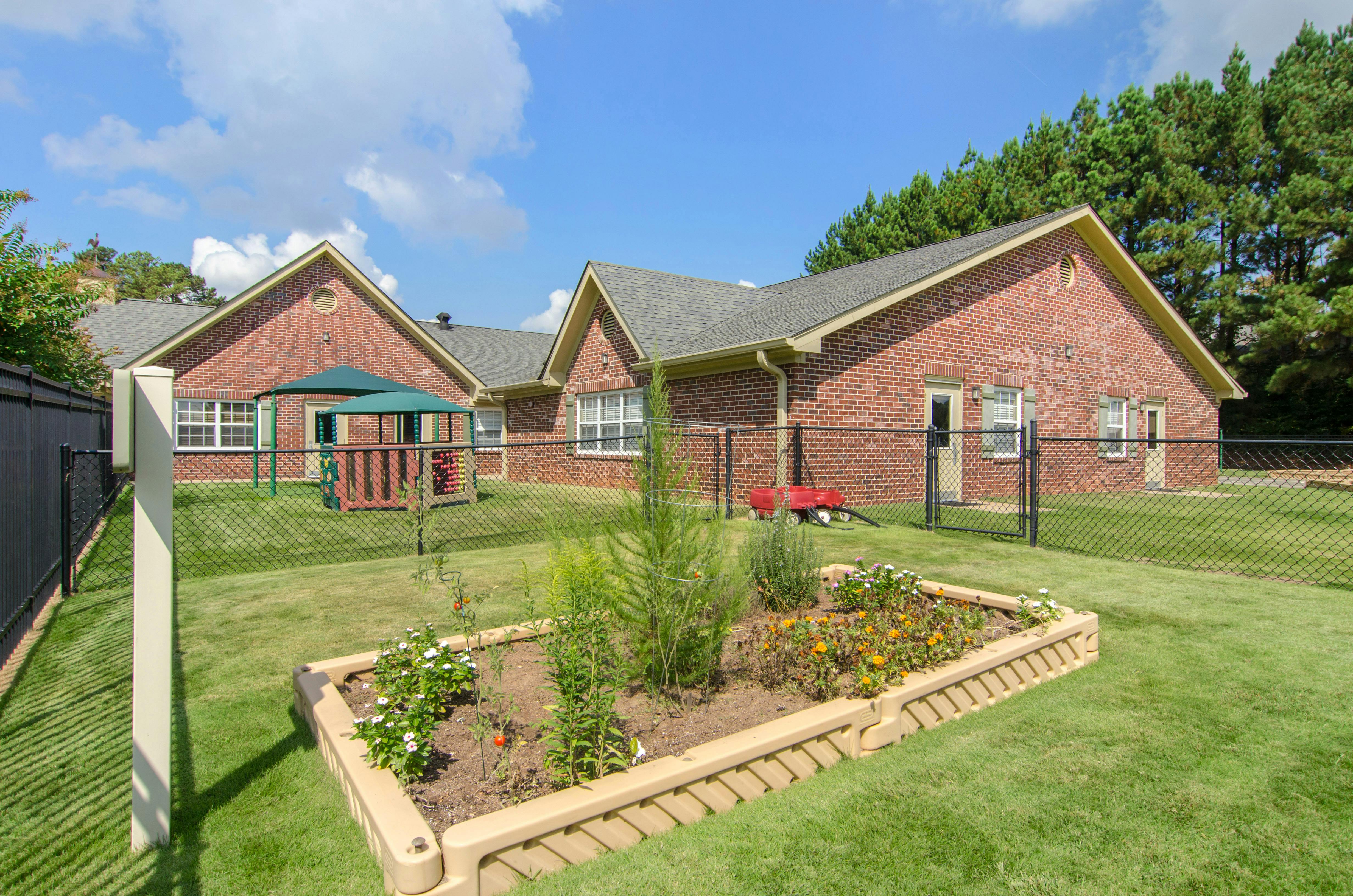 Brick building with a fenced playground and garden bed in the foreground