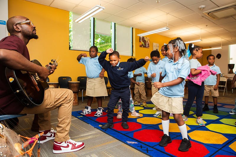Person playing guitar for children dancing in a classroom