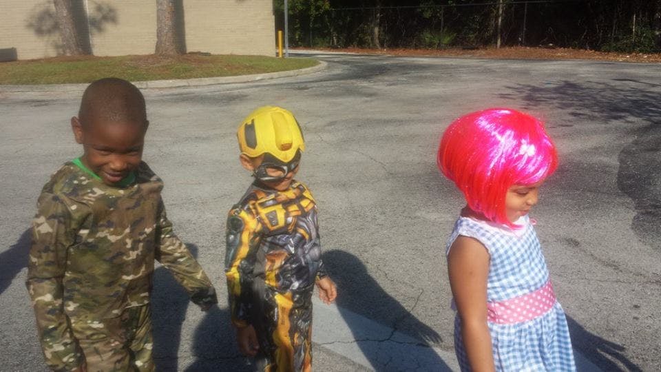 Three children in costumes, one in camouflage, one in a robot suit, one in a pink wig