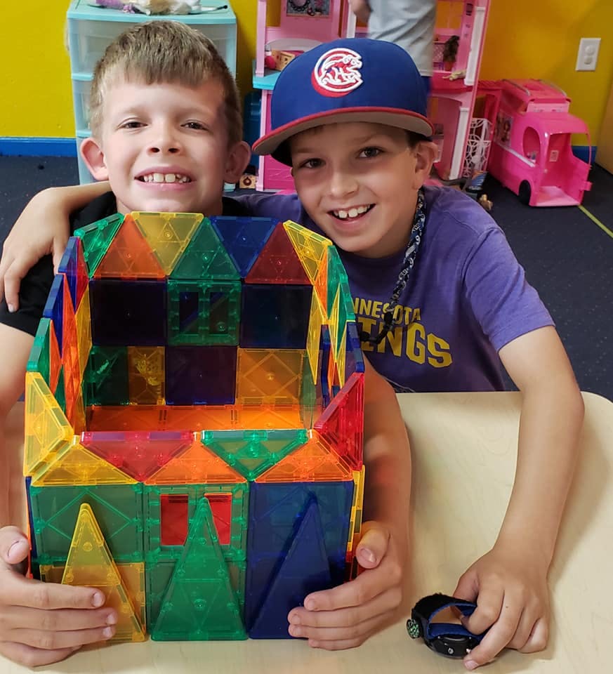 Two children smiling, one holding a colorful magnetic block structure