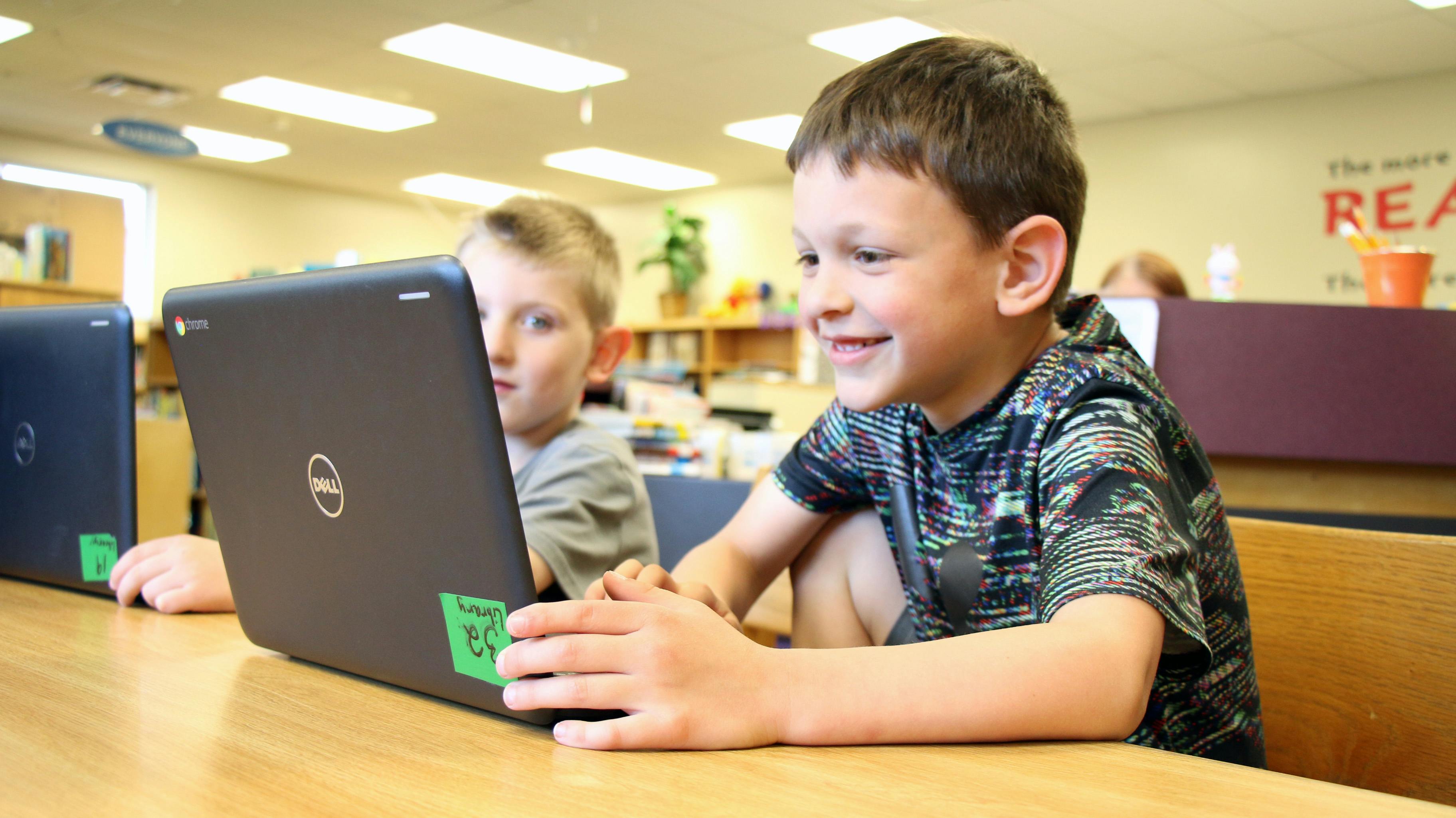 Two children using laptops in a classroom