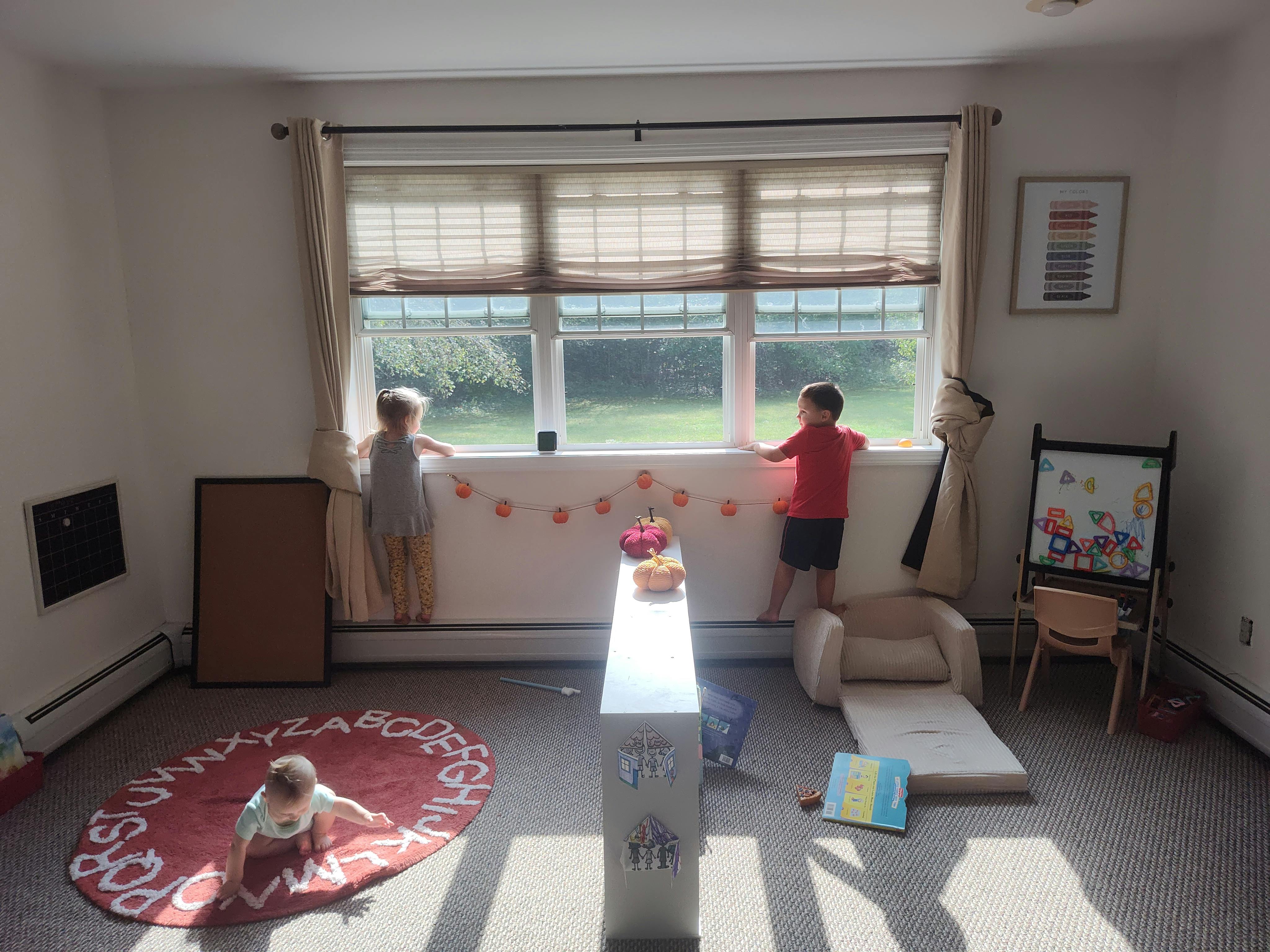 Two children looking out a window, one child on a rug