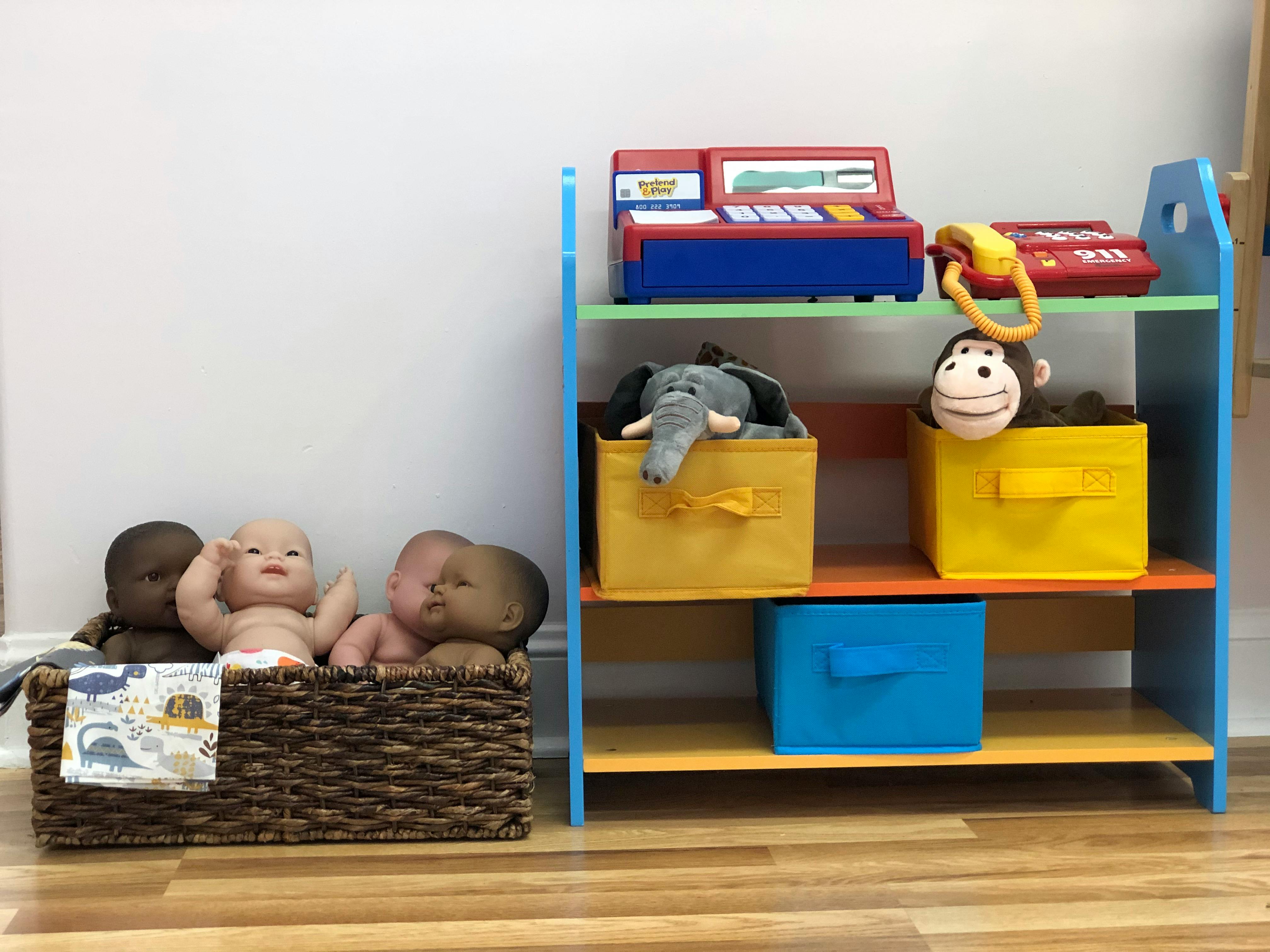 Dolls in a basket next to a toy shelf with stuffed animals and toys