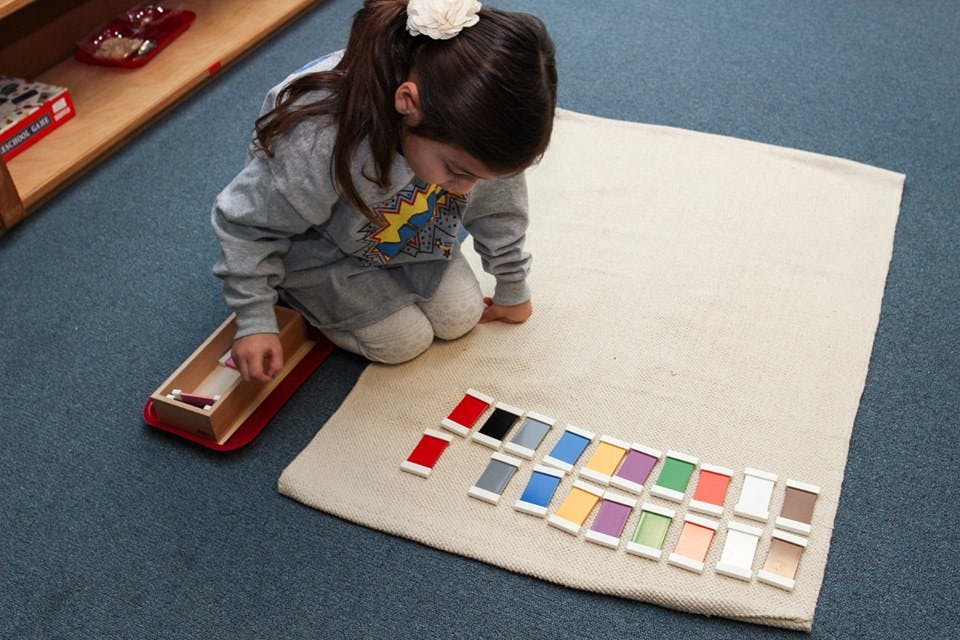 Child kneeling on floor, arranging colorful blocks on a mat