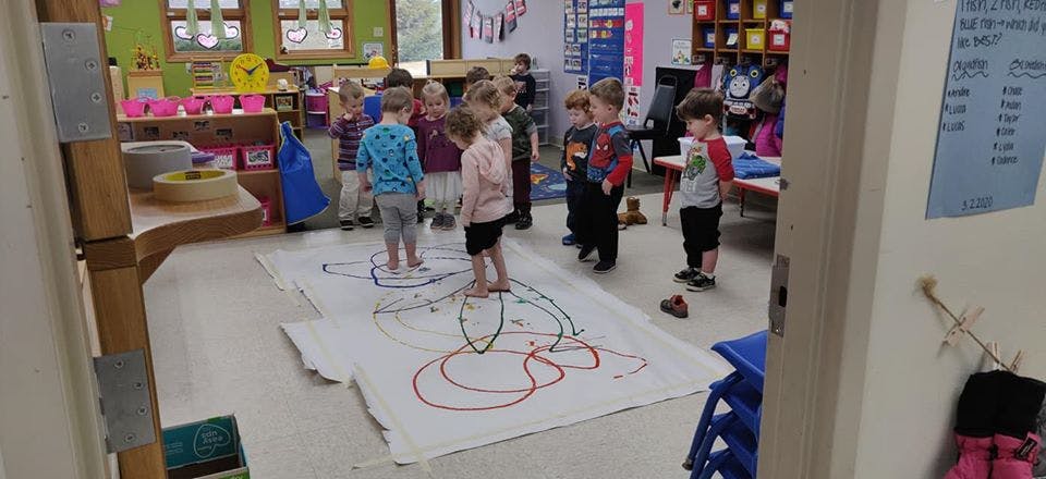 Children standing on a large drawing in a classroom