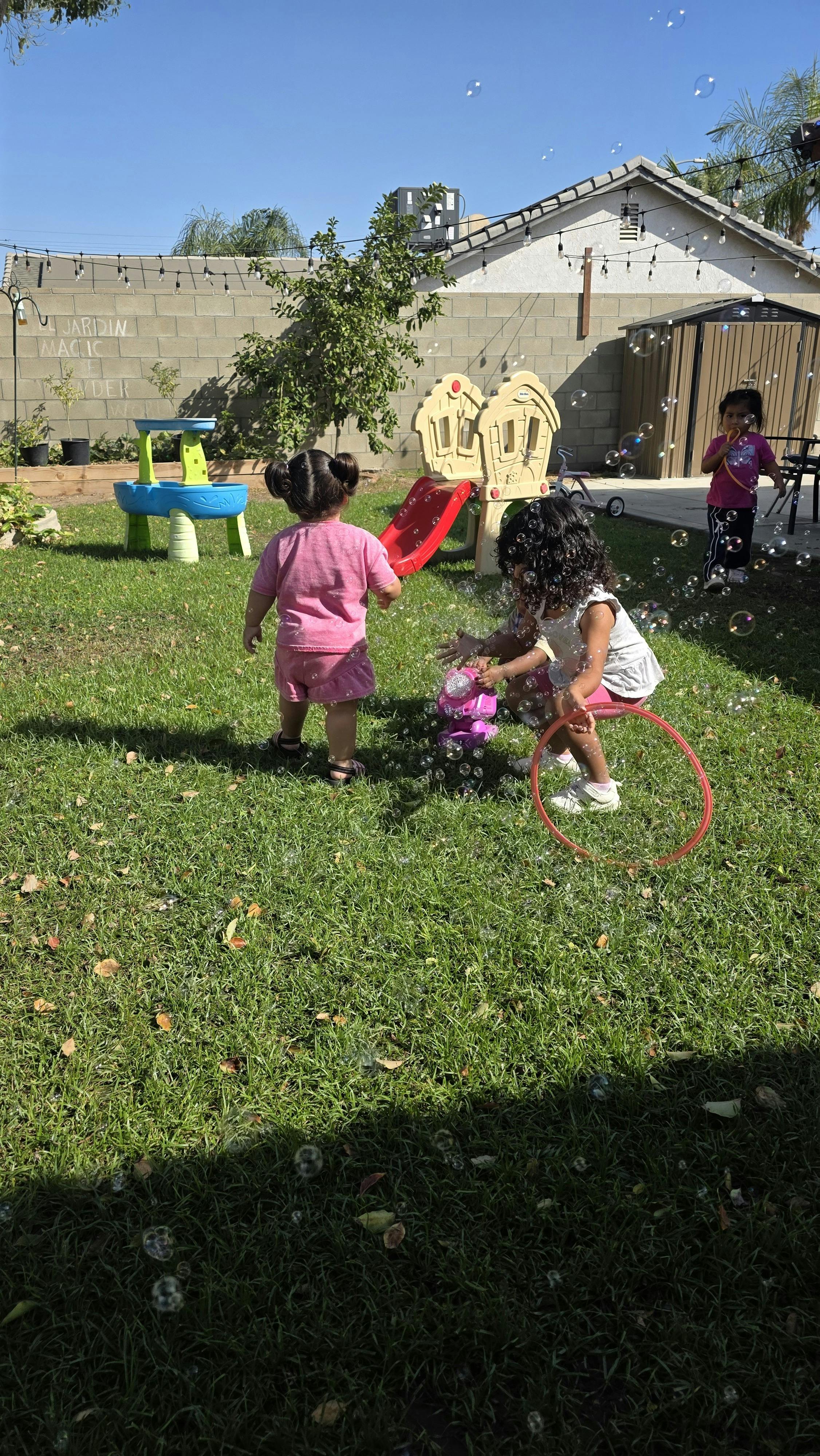 Three children playing with bubbles in a backyard