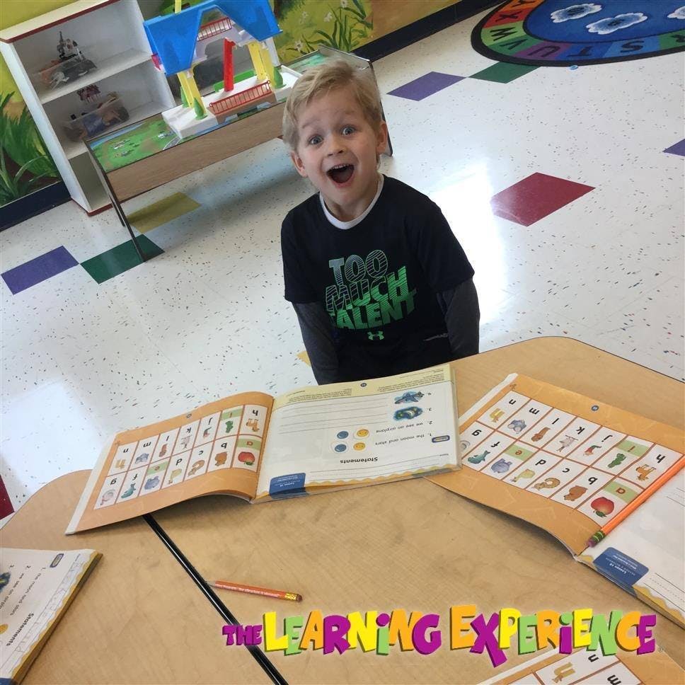 Child looking up from a desk with open books in a classroom