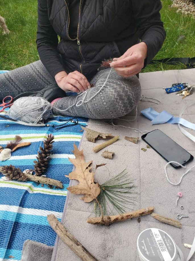 Person sitting on ground, holding yarn and crafting with natural materials