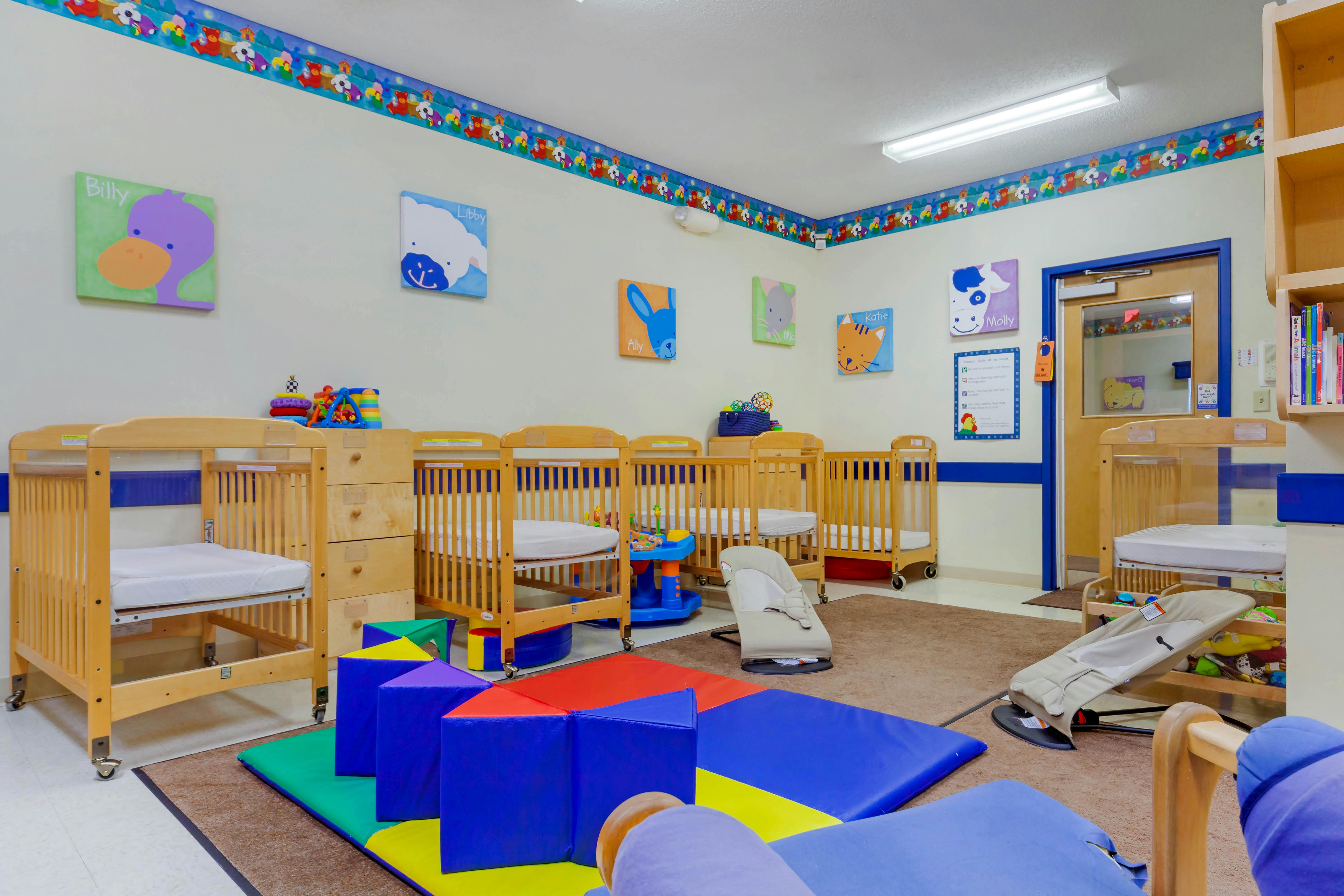 Baby room with multiple wooden cribs, colorful play mats, and animal wall art