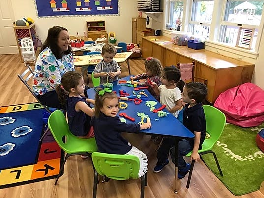 Person and children at a table with playdough in a classroom