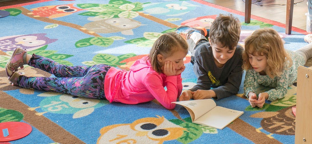 Three children lying on a rug looking at a book