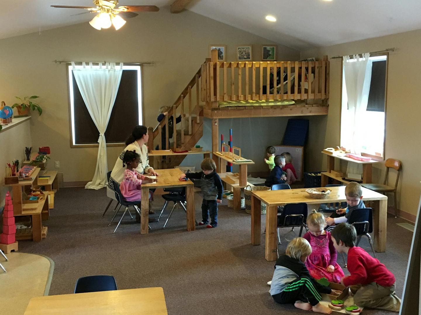 Adult and children in a classroom with tables and a wooden play structure