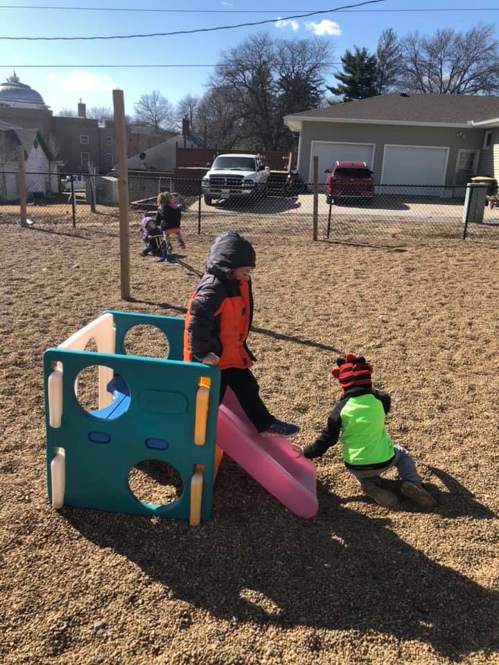 Two children playing on a small slide on a playground