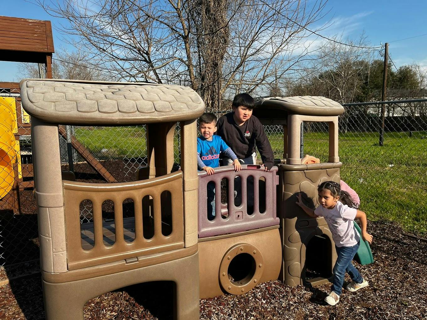 Three children playing on a plastic playground structure outdoors