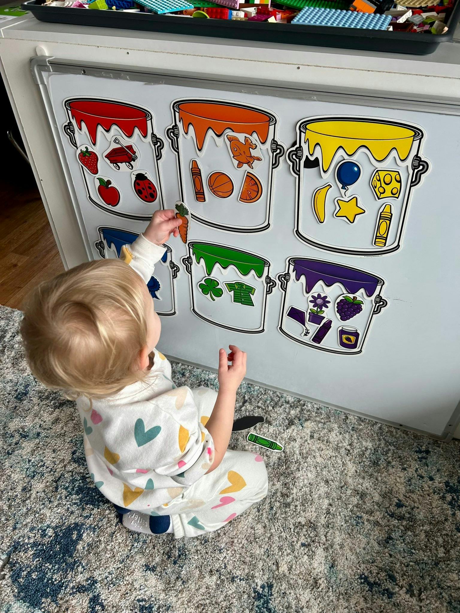 Child placing a sticker on a whiteboard with color-themed paint bucket graphics
