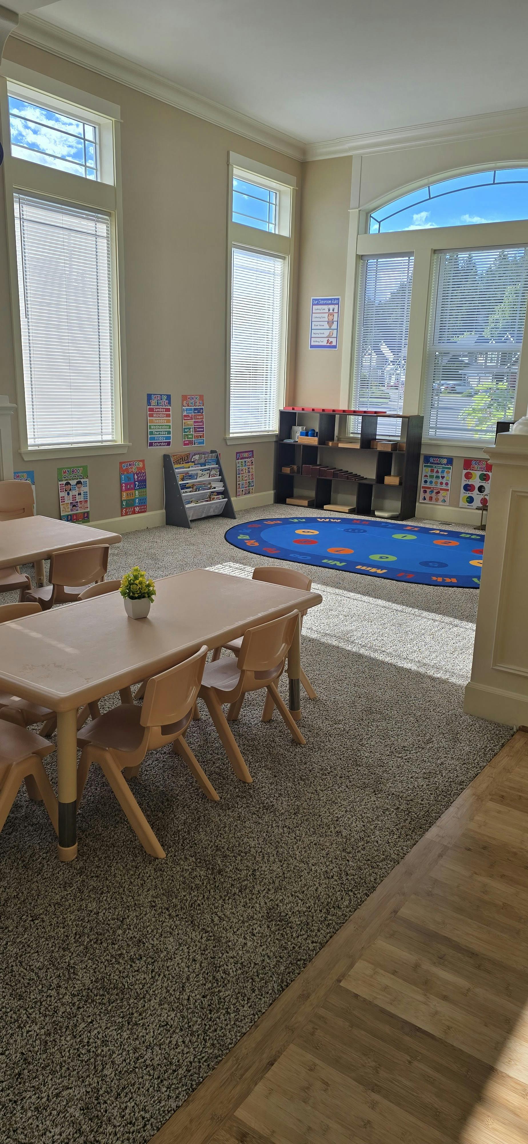 Classroom with tables, chairs, a rug, and educational posters on the walls