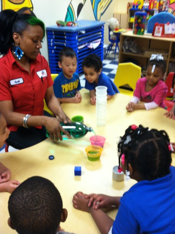 Person pouring liquid from a bottle into cups for children at a table